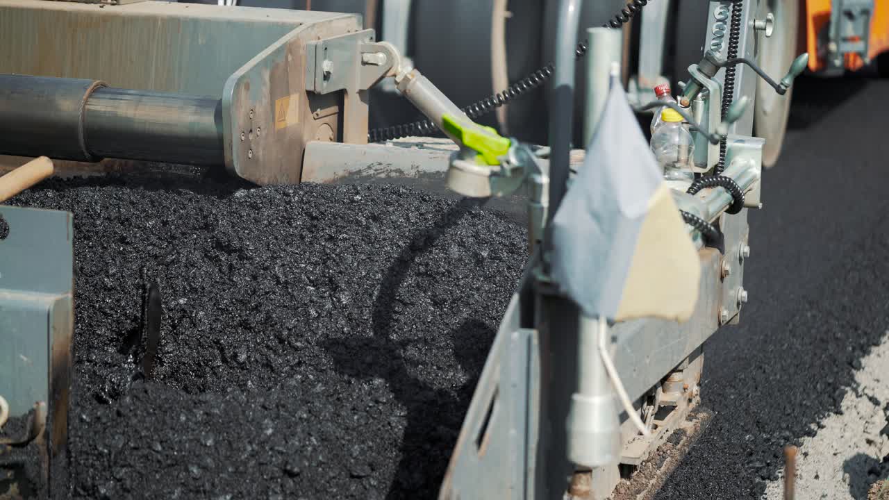 professional equipment is mixing bitumen and putting the mixture on the road on the background of a passing roller machine