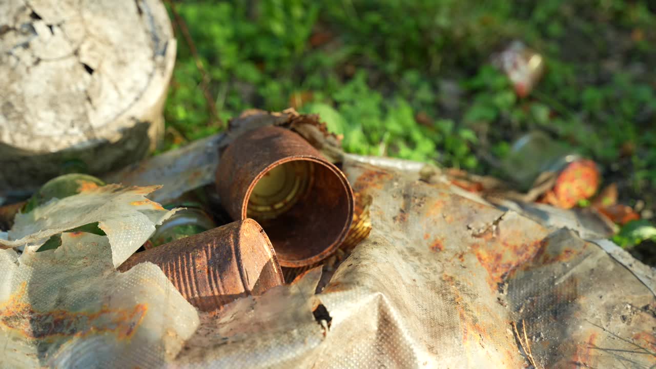 Close-up of rusting cans and dirty plastic in forest. Human impact on environment