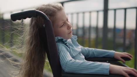 schoolgirl with paralysis sits in wheelchair looking at city