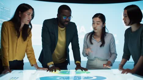 a diverse group engages in collaborative discussion around an interactive digital table, analyzing data and exploring innovative solutions together