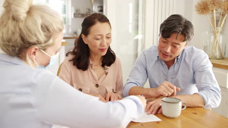 mature asian couple at home meeting with female financial advisor in mask during pandemic and signing document- shot in slow motion