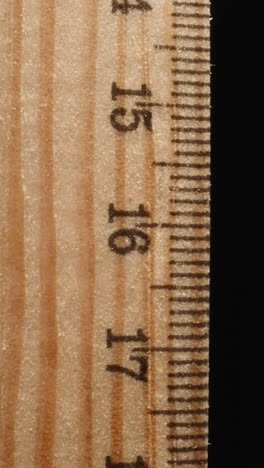 wooden ruler marked with digits turning on black background. straight strip from wood designed for drawing lines or measuring distances macro