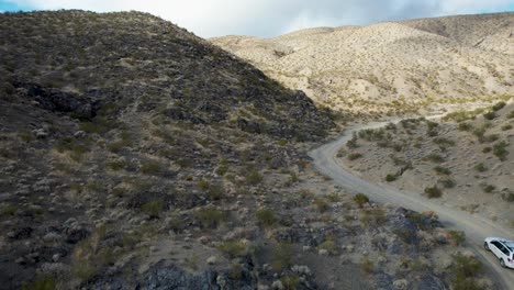 Weißes-Auto-Fährt-Abseits-Der-Straße-Mit-Panoramablick-Auf-Felsige-Wüstenhügel