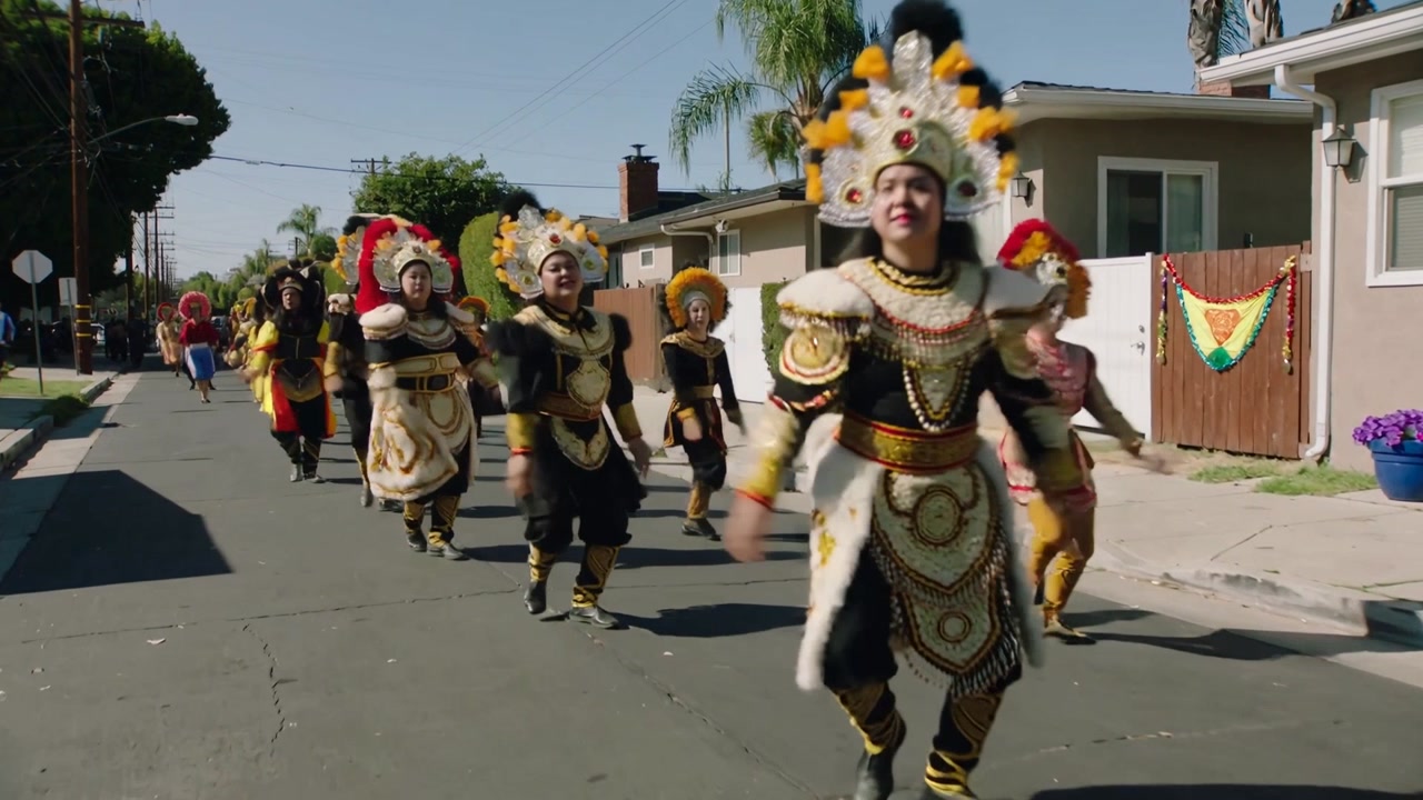 Marching troupe advancing on sunlit street, parade starting, moving in sync, showing feather crowns