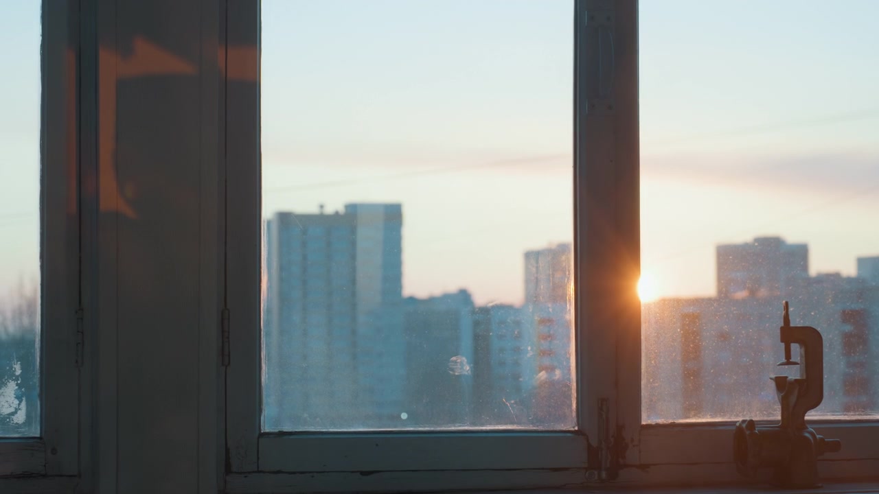 Sunrise over city skyline through window warm golden light filters through dusty glass onto windowsill hint of tutor study scene with notebook and pen calm home coaching atmosphere quiet morning