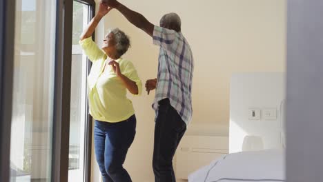 Happy-senior-diverse-couple-dancing-in-living-room-at-retirement-home