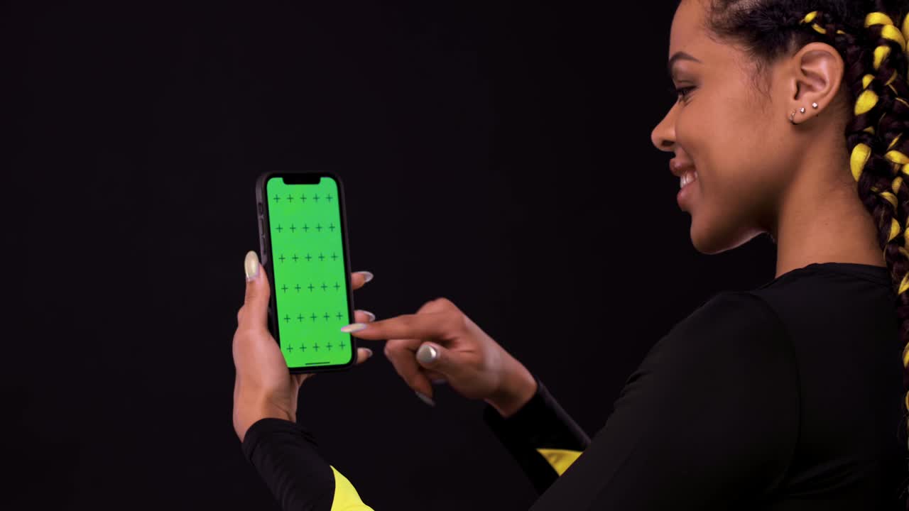 retrato de una chica afroamericana sonriente apuntando con el dedo a la pantalla del teléfono móvil con una llave cromática. mujer aislada sobre un fondo negro