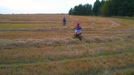 couple riding motorbikes in the field with mowed grass. young people having fun spending time actively in the nature at the end of the day.