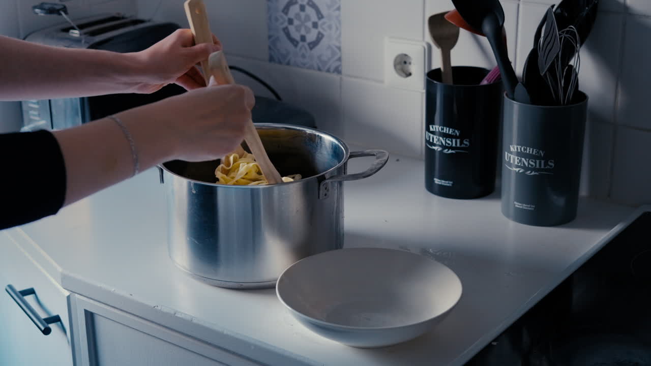 mujer poniendo tagliatelle de pasta de la olla en un plato con dos cucharas de madera en una cocina blanca en cámara lenta durante un día