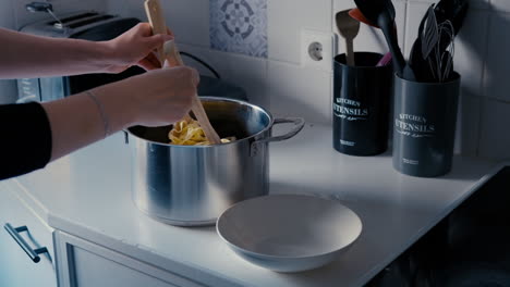 mujer poniendo tagliatelle de pasta de la olla en un plato con dos cucharas de madera en una cocina blanca en cámara lenta durante un día
