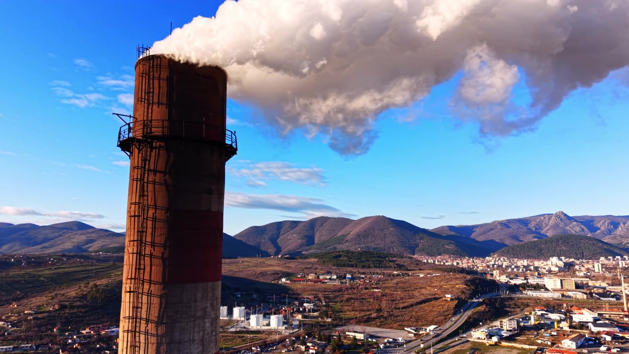 Panorama montano con periferia cittadina e zona industriale, Bulgaria. Ampia vista elevata di dolci crinali montuosi spogli sotto un cielo blu con nuvole sparse, edifici cittadini e serbatoi di stoccaggio a destra.