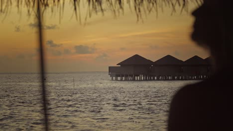 bungalows sobre el agua en las maldivas durante la puesta de sol con la silueta fuera de enfoque de la mujer