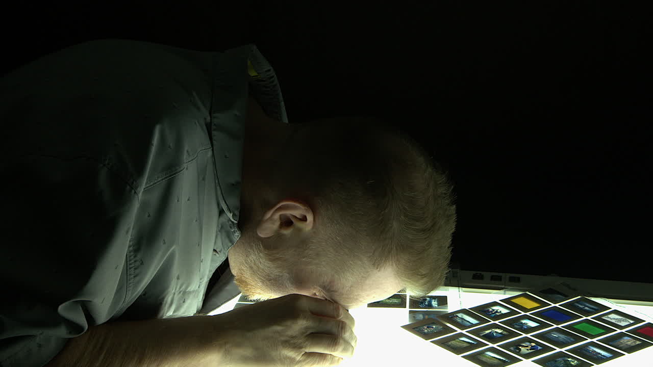 Man selects film slide to view on illuminated light box in dark room