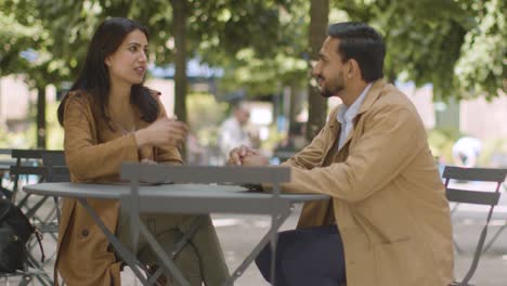 muslim couple on date sitting at outdoor table on city street talking together