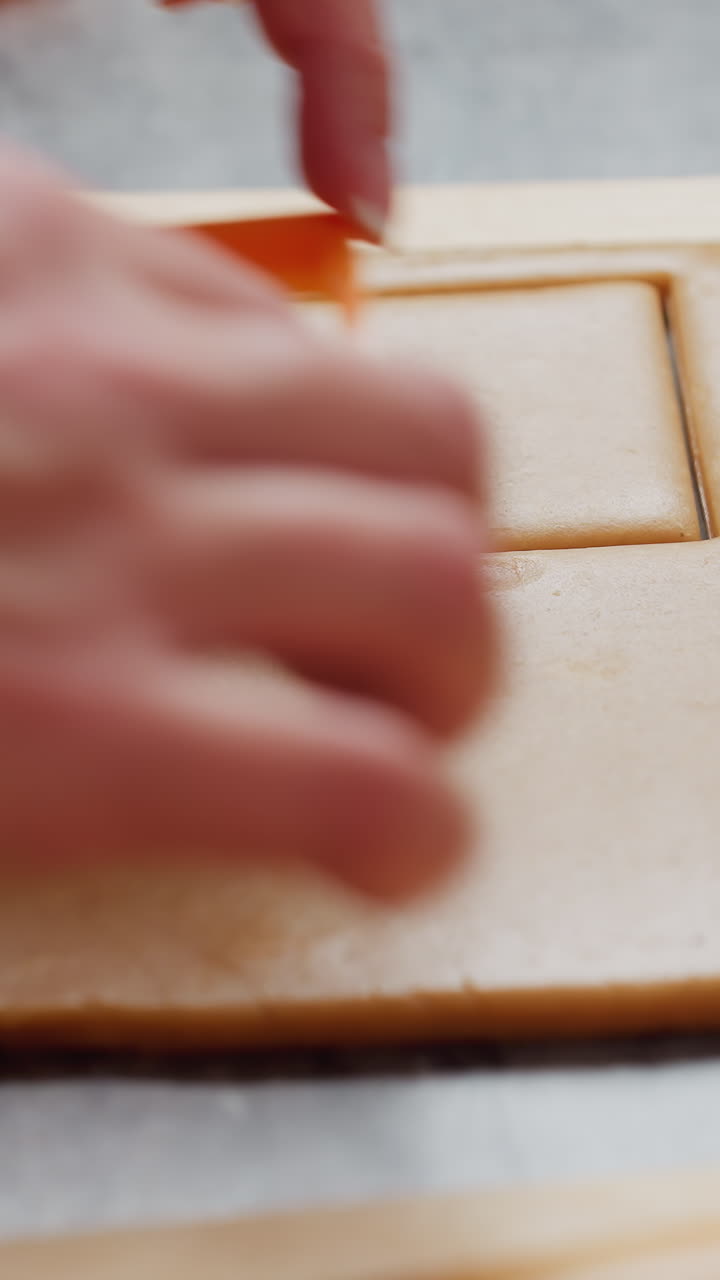 primer plano de las manos del panadero presionando un cortador de forma naranja en una masa marrón lisa, rodillo de madera y otras herramientas de panadero descansan cerca en la encimera texturizada