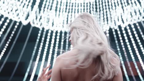 beautiful blonde woman in a red evening dress filmed from below. bright lights above her. beautiful movements