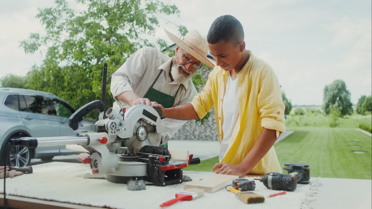 el mayor enseña a un adolescente cómo usar una sierra circular en un taller de jardín