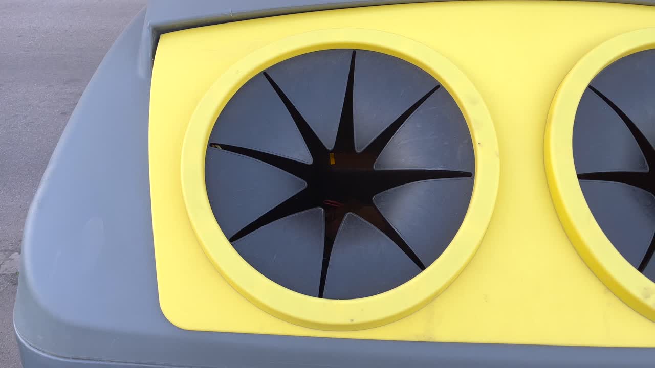 뒤에 도로가 있는 플라스틱을 위한 노란색 재활용 컨테이너의 입구