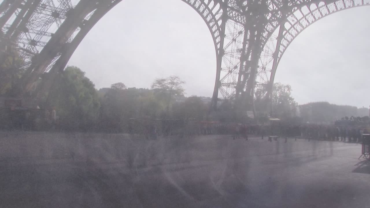 Visitatori che arrivano attraversando la piazza sotto l'arco della Torre Eiffel, fermandosi alle ringhiere per scattare foto per il turismo.
