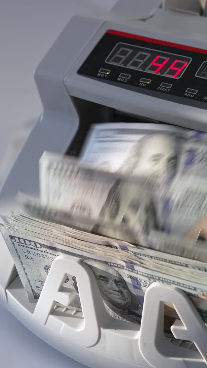 Male puts a wad of US dollars into money machine. Equipment for financial operations working. High angle view. Close up. Vertical video
