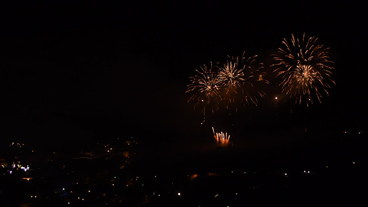 Celebration with many golden and sparkling fireworks, over a mountain town, at night