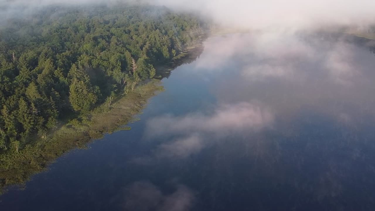 Lake in early morning with low hanging, misty clouds in remote mountain forest