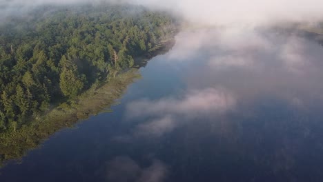 Lake-in-early-morning-with-low-hanging,-misty-clouds-in-remote-mountain-forest