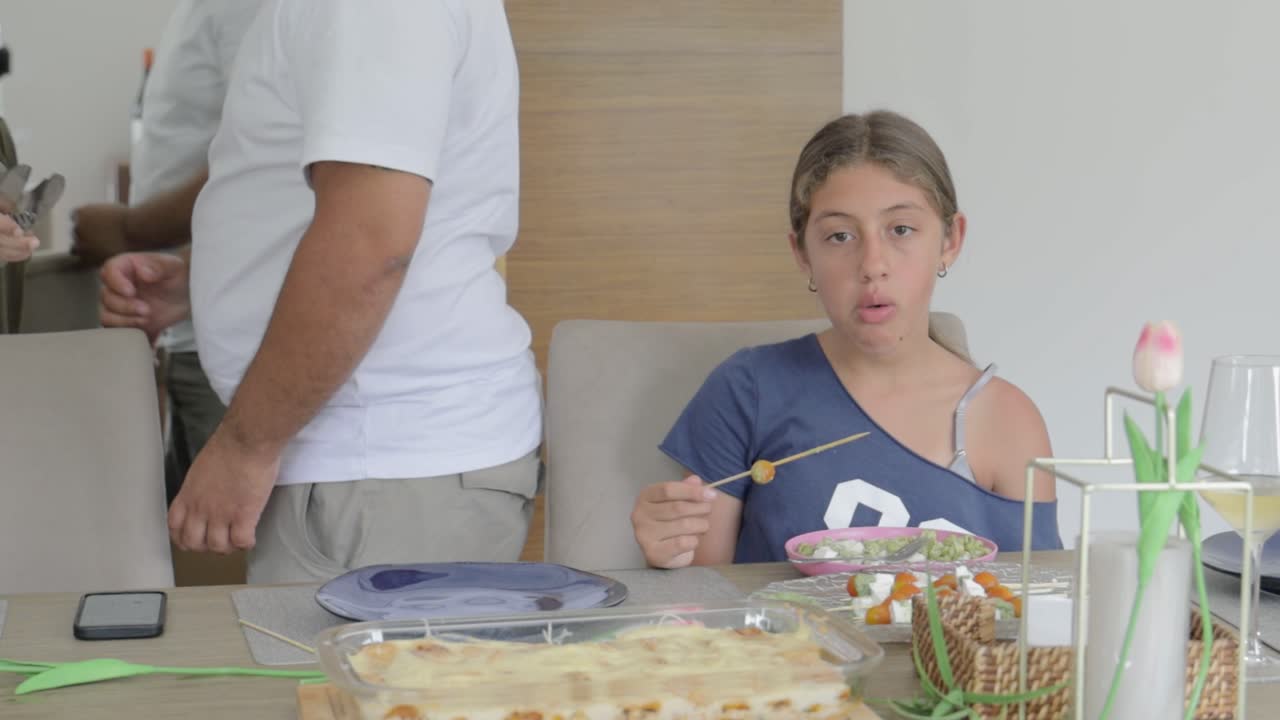 Aile üyeleri yemek hazırlarken yemek masasında yemek yiyen genç kız.