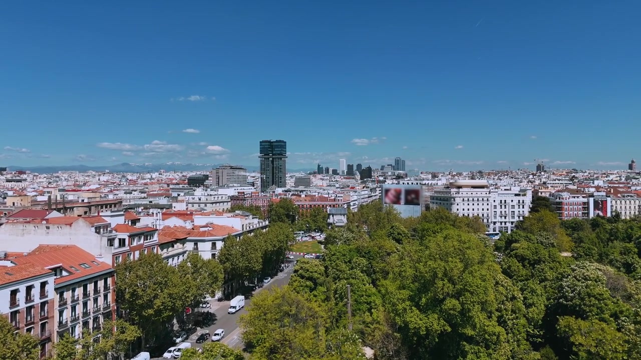 Ripresa con drone sui tetti del centro di Madrid con parchi e torri sotto un cielo blu.