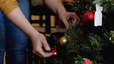 woman hands placing yellow ball ornament setting up christmas tree with lights tight shot