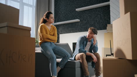 couple rest moving house feeling exhausted. spouses sitting couch with boxes.