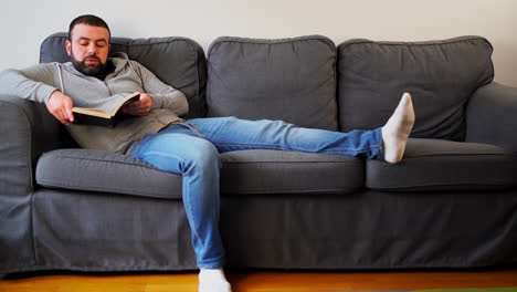 man leaning comfortably on sofa while reading book