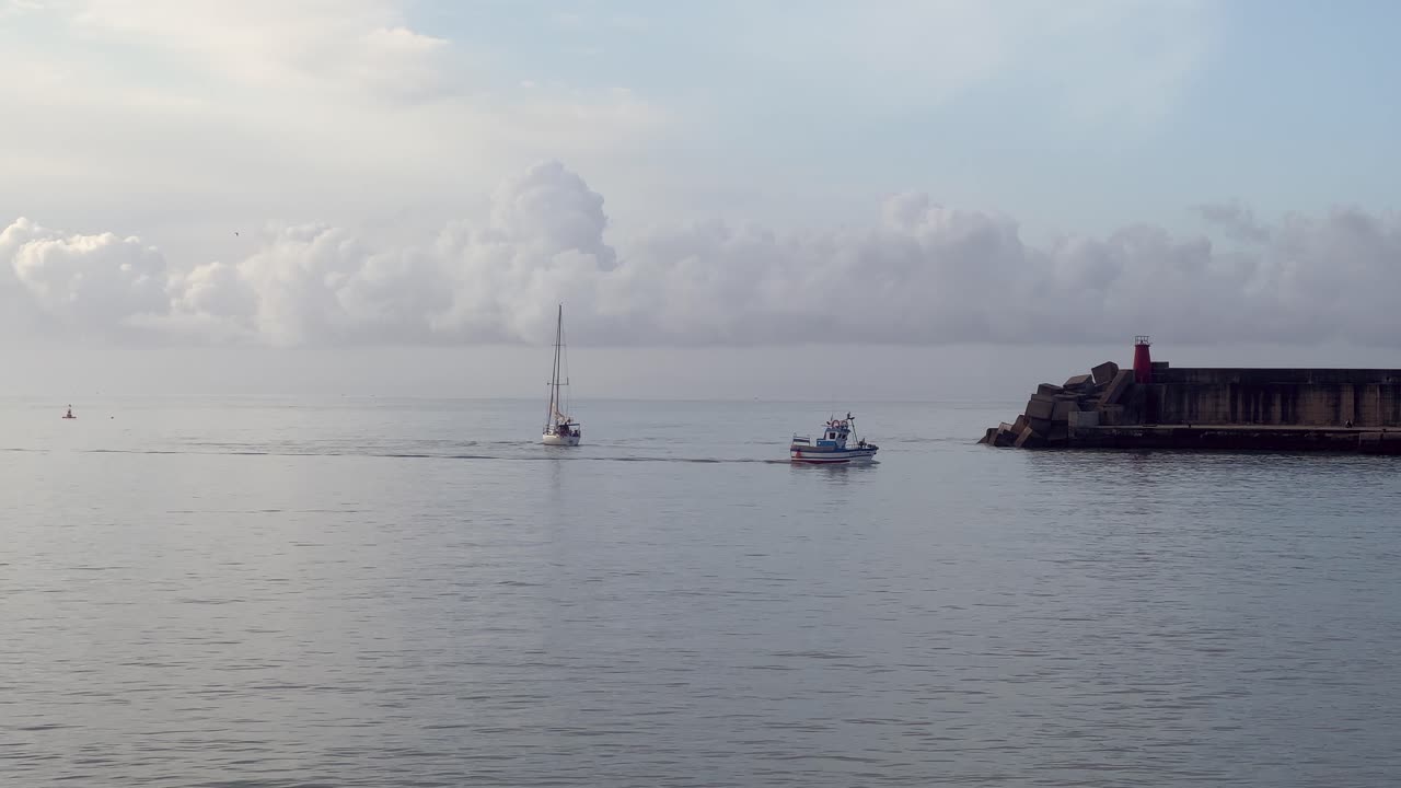 Static view of a crossing between a sailing boat and a fishing boat near the coast.