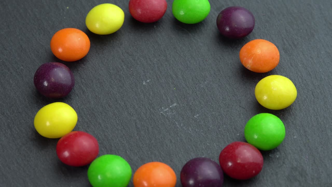 los dulces de colores giran sobre un fondo negro y la mano toma un dulce, dulces de color