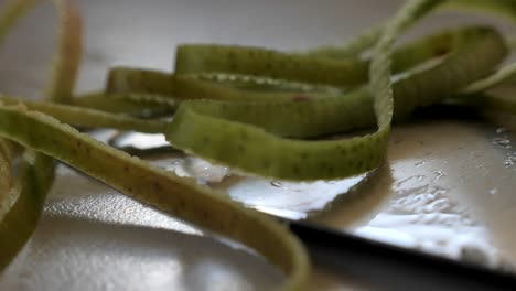 sartén a cámara lenta sobre un cuchillo afilado de metal con cáscara de manzana verde que lo cubre y gotas de agua