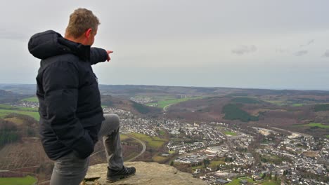 Das-Sauerland-panorama:-Ein-Senior-Mann-In-Einer-Schwarzen-Jacke-Zeigt-Nach-Einer-Langen-Wanderung-An-Einem-Bewölkten-Tag-In-Die-Ferne-Auf-Den-Olsberg