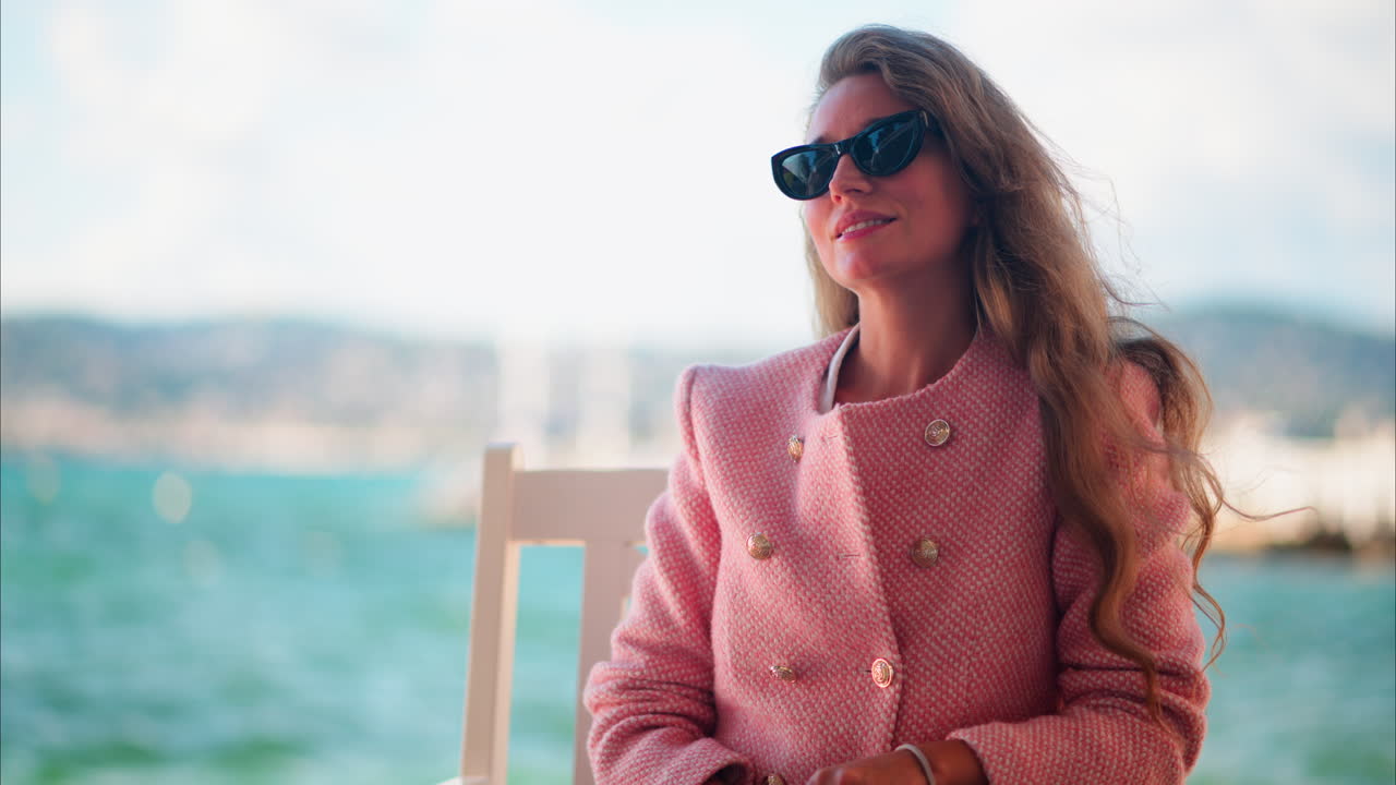 Kvinde i en lyserød blazer, der sidder på en stol på stranden i Antibes, Frankrig