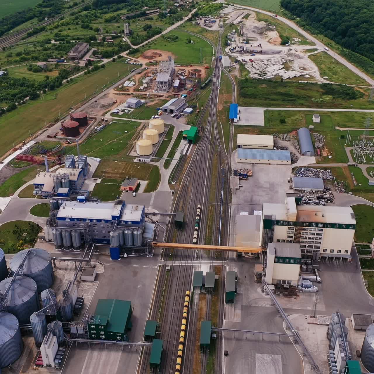 Huge territory of the modern granary complex. Railways and cargo trains in the middle of plant territory. Green fields and forests at the backdrop