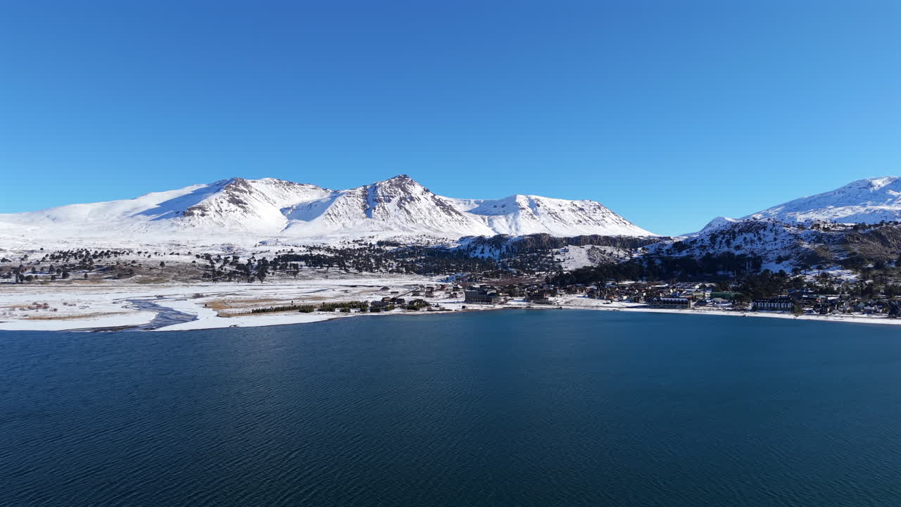 Wide drone view of Lake Caviahue with the snow-capped peaks of the Andes in the background, near the Copahue volcanic complex, highlighting Patagonia’s winter scenery and mountain landscapes