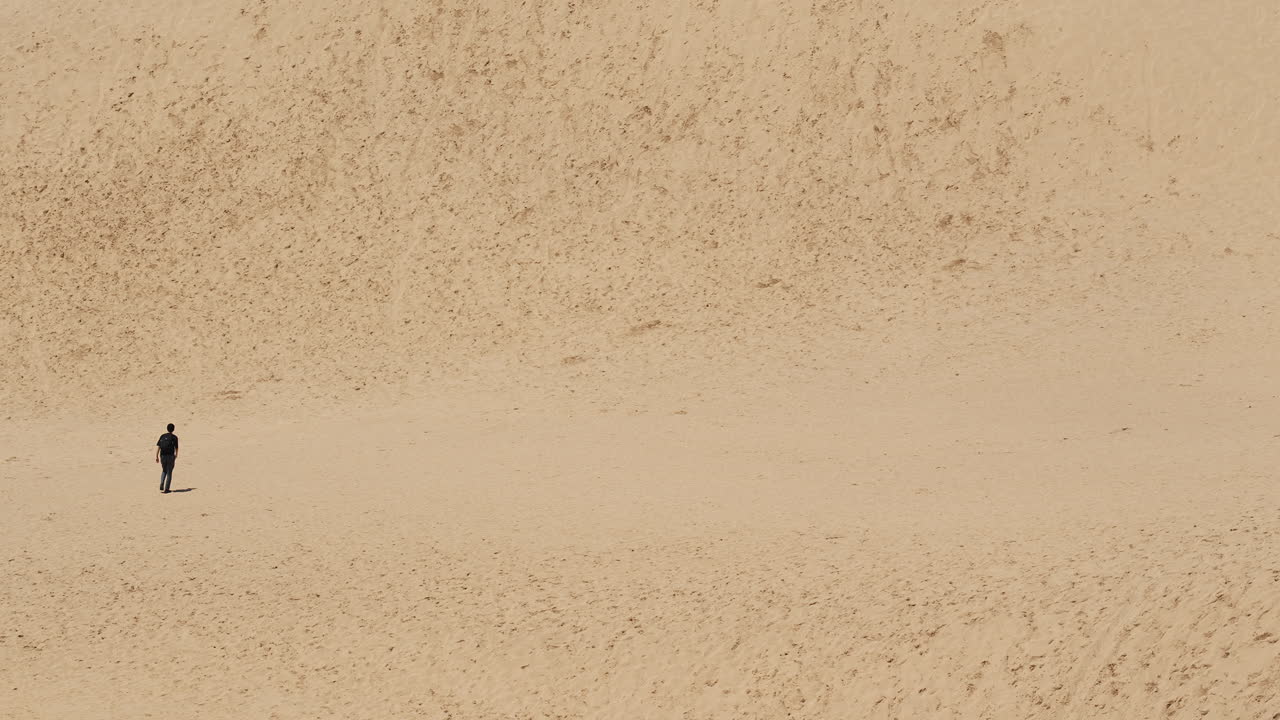 Lone traveler traversing serene sand hills against clear horizon