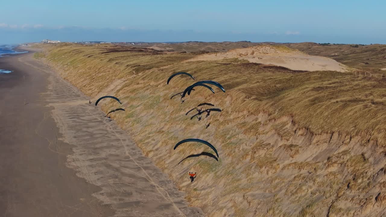 Group of paragliders soar along grassy sand dune slopes of Castricum beach, Netherlands