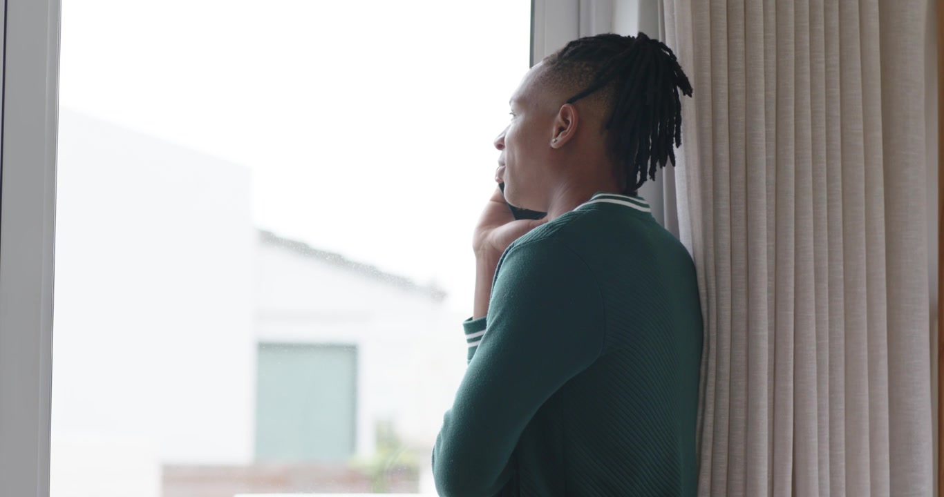 Homme afro-américain penché à droite à la fenêtre, prenant un appel, tenant son téléphone, écoutant, espace pour texte