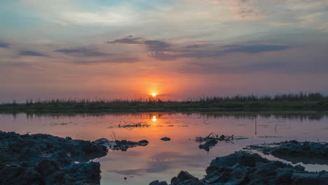 golden sunset over okavango delta with wispy clouds reflection on calm waters in botswana - time lapse