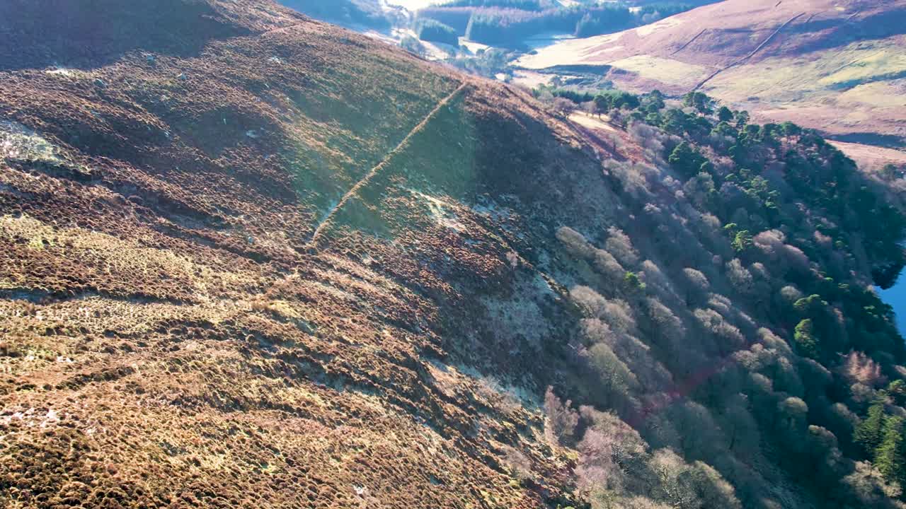 una lenta toma aérea de la tarde del lago guinness o lough tay con agua azul y negra como el cristal en un día soleado de enero mientras las sombras se extienden