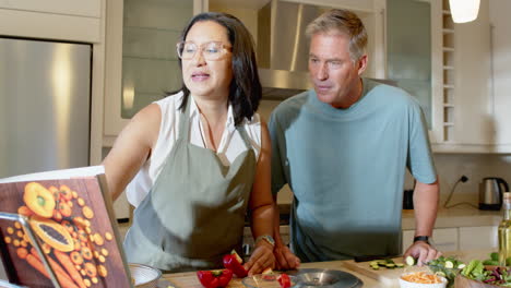 senior diverse couple cooking together in kitchen, following recipe from cookbook, smiling, at home