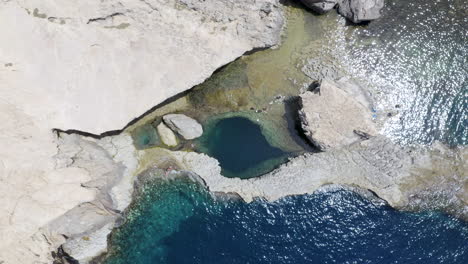 Gente-Nadando-En-La-Laguna-De-Mar-Rocoso-Debajo-De-La-Ventana-Azul,-Malta,-Arriba