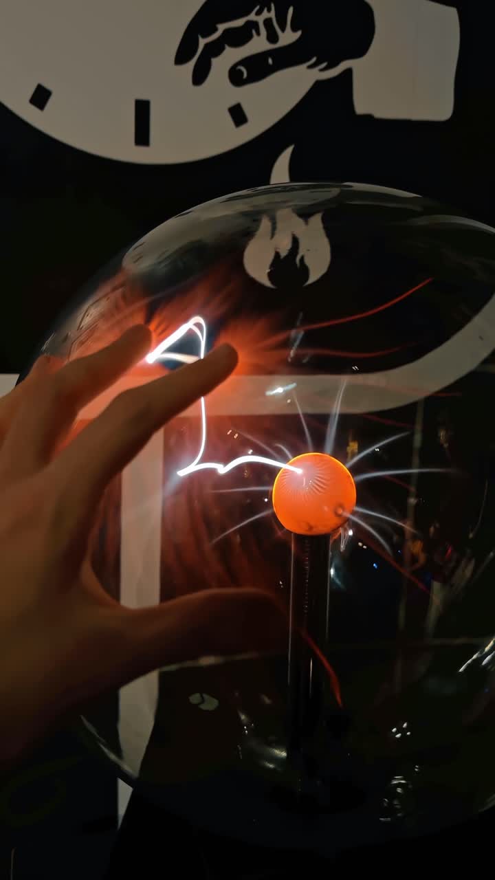 New York, USA, 25 April 2025: Hand Touching Plasma Globe With Electric Arcs. Hand near plasma globe with orange electrode, white arcs, red filaments, dark indoor background