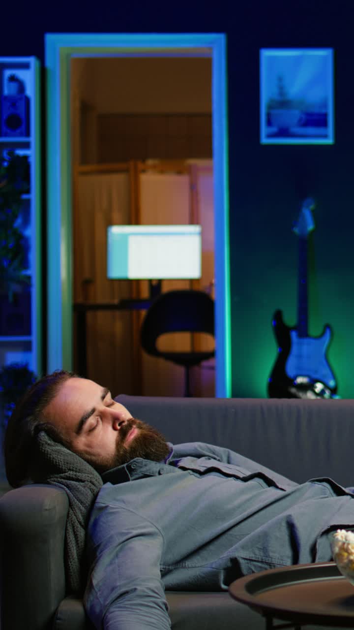 Vertical video Exhausted man sleeping on couch after working on laptop and watching TV
