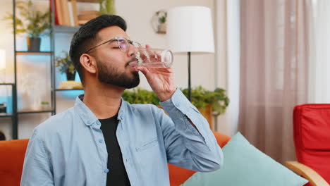 indian ill sick man taking medicine antibiotic pill with water at home sofa health care pharmacy