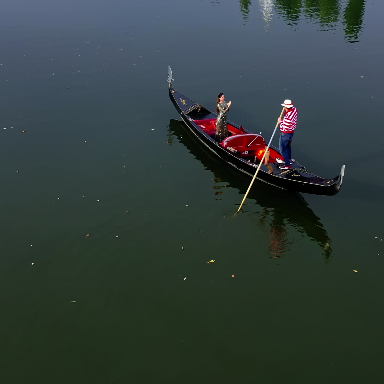 Gondolier riding a boat with a woman. Beautiful lady travelling in gondola along the river at sunset. Aerial view. Camera motion around.